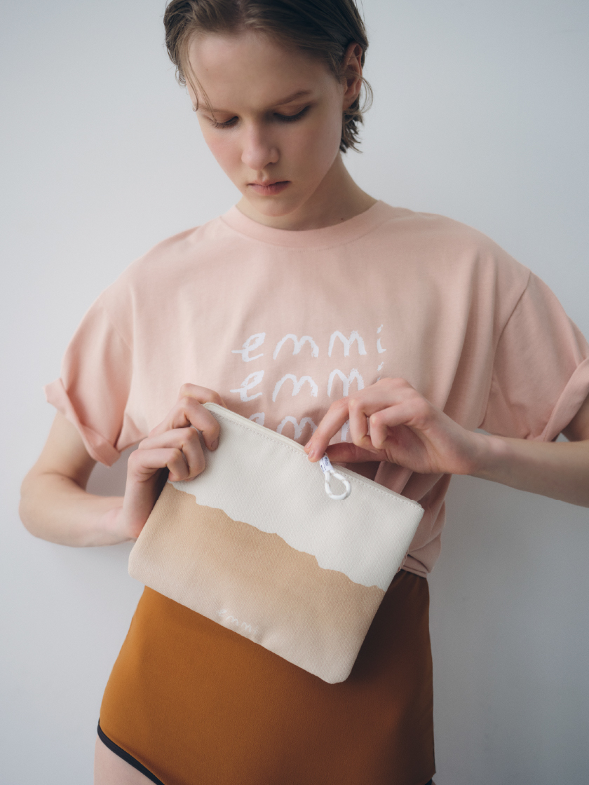 【emmi×ecostore】UpDRIFT emmiロゴTシャツ・スカーフ付きスイムウェアを着用し、【emmi×ecostore】eco フラットポーチを手に持った女性