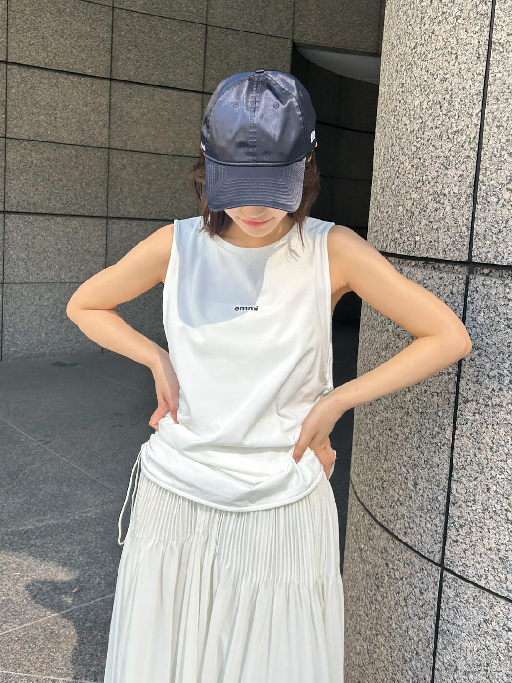 白色のeco サイドドロストタンクとシアピンタックフレアスカート、ネイビー色の【emmi|NEW ERA®】9TWENTY™サテンキャップを着用したモデル画像