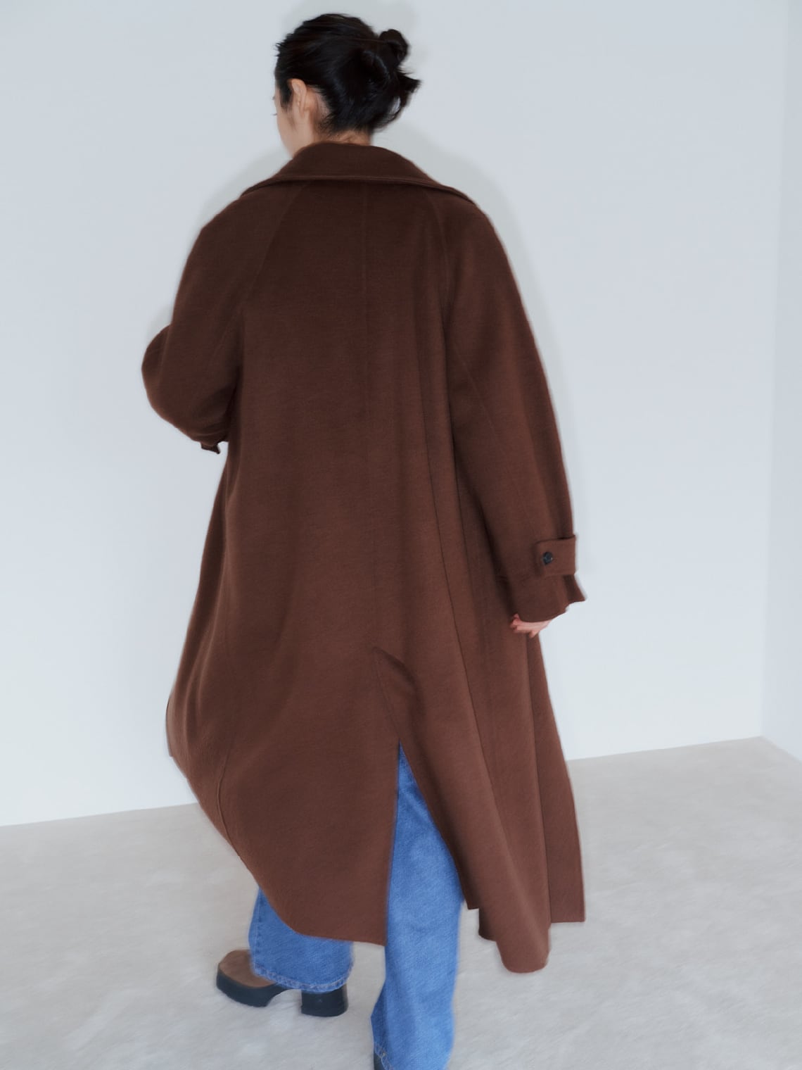 ブラウンのロングコートにゆったりとしたデニムのパンツを穿いた女性の後ろ姿