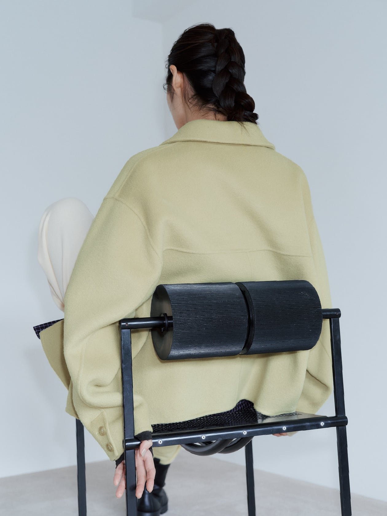 ライトオリーブ色のジャケットを羽織って椅子に座っている女性の後ろ姿