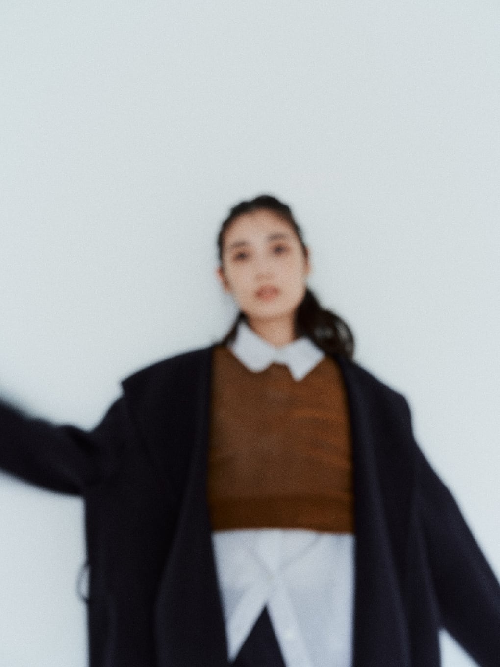 ネイビーのウールコートとブランのトップスを着た女性の手ぶれ写真