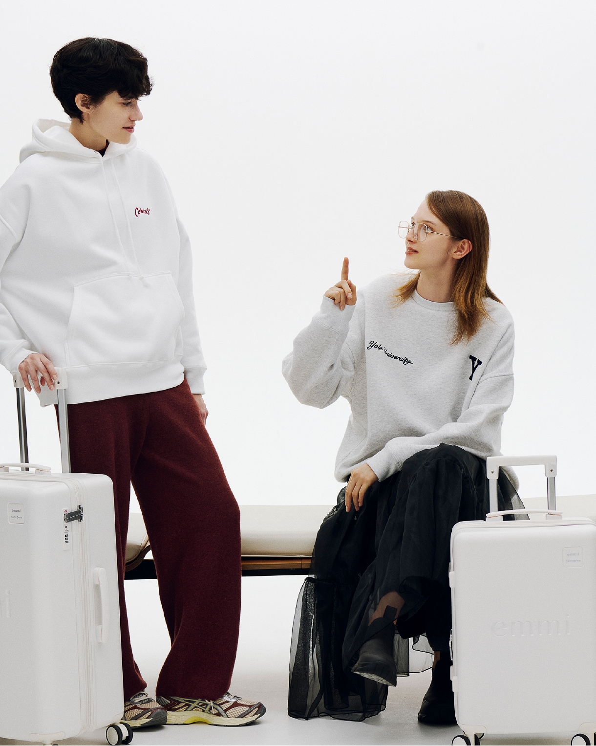 スーツケースを持って談笑する男女のイメージ画像（着用アイテムは下クレジットに記述）