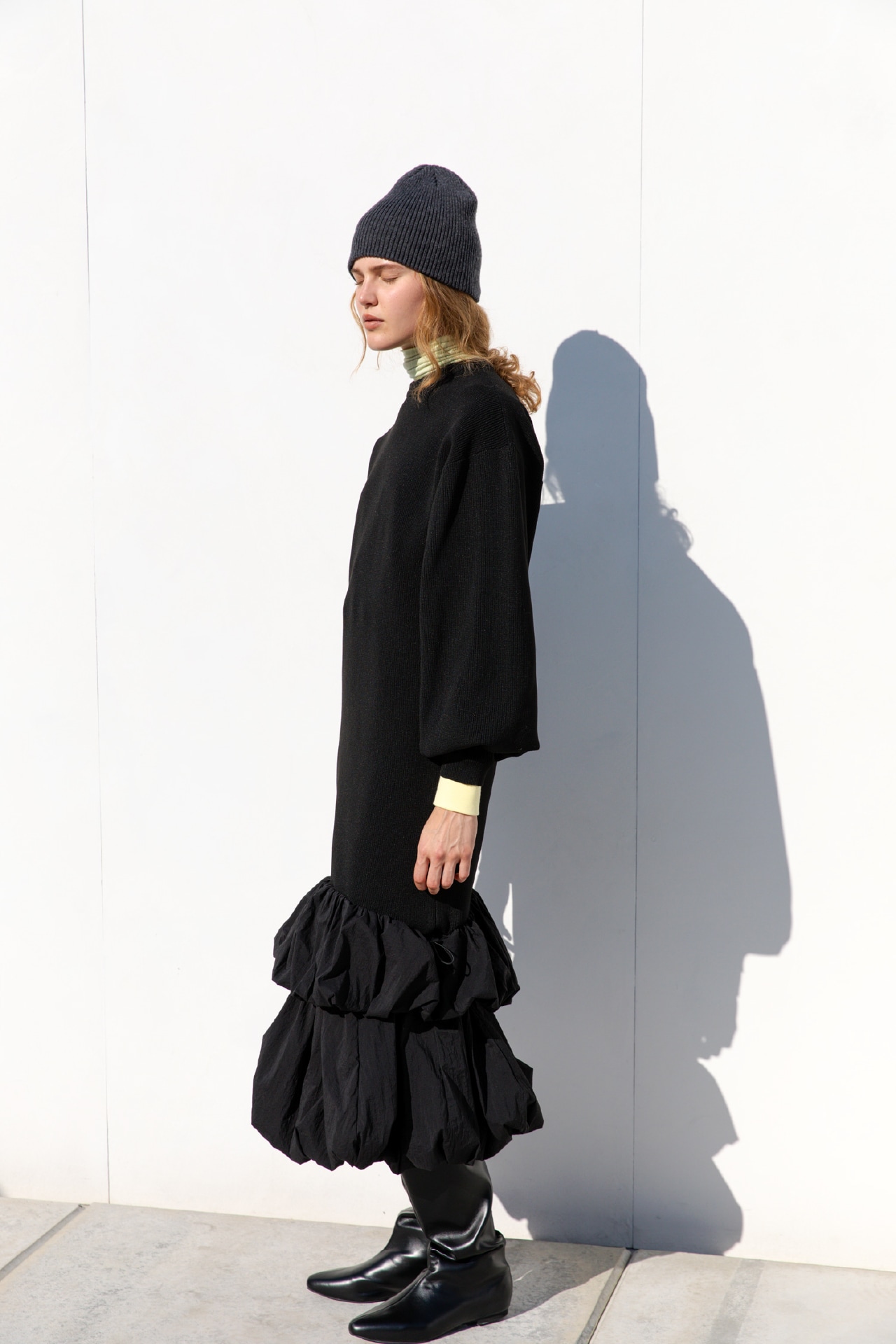 黒のニットタフタドッキングOP・LIMEのハイネックカットソー・イエローのエンブロイダリーemmiロゴスウェット・ダークグレーのウールリブニットビーニー・黒のインヒールジョッキーロングブーツを合わせたバストアップ写真