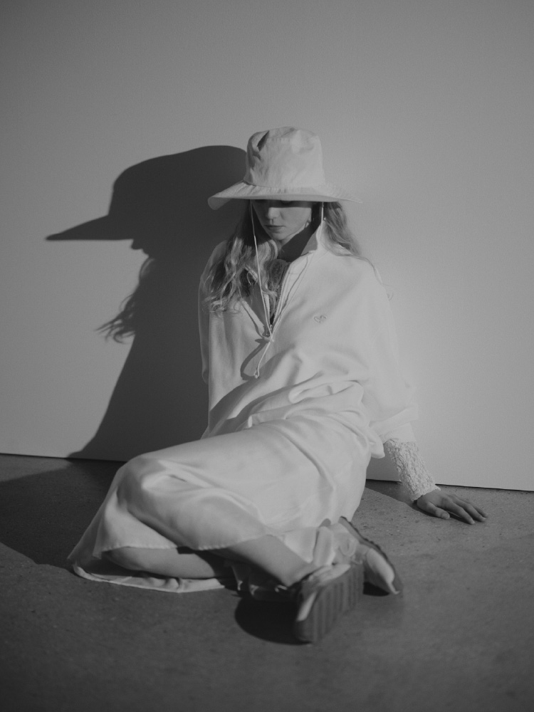 【em】ハーフジップスウェット【セットアップ対応】、2wayストレッチレースカットソー、サテンナロースカート【セットアップ対応】、サンガードアウトドアハット/撥水/UVカット、【em】メリージェーンスニーカーを着用して床に座ってる女性のイメージ