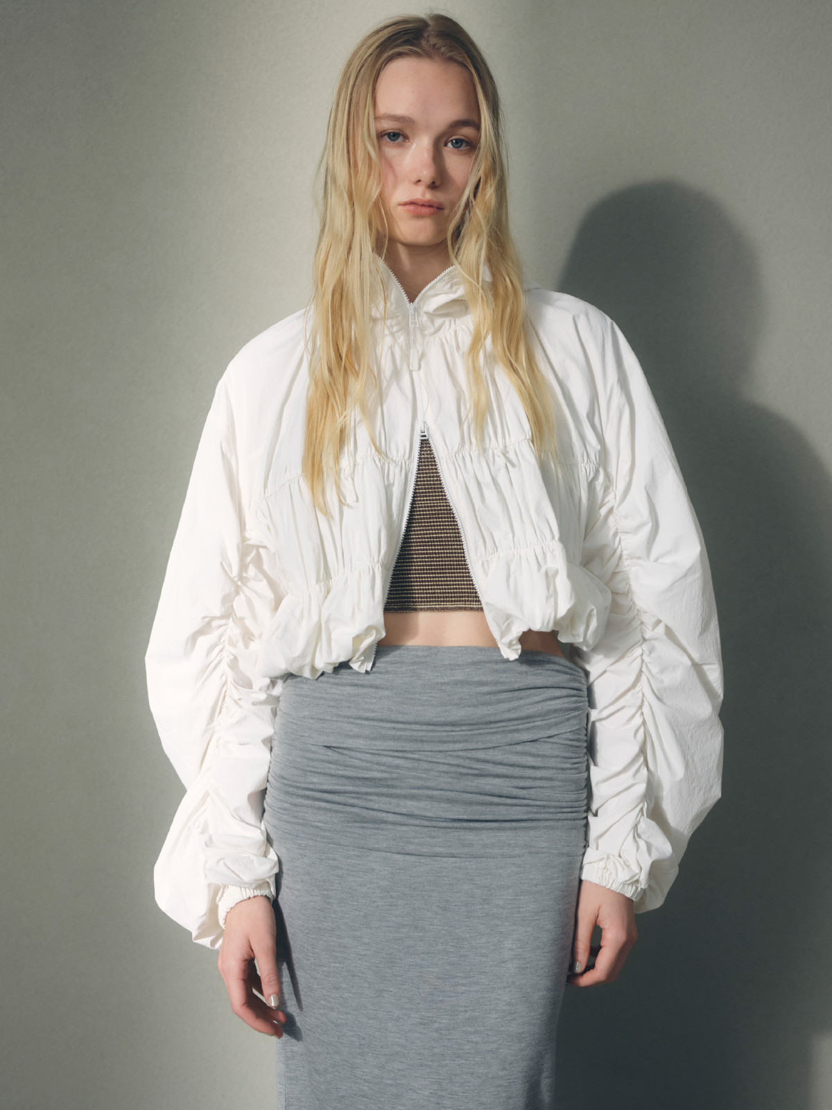 白色の【Movique】シャーリングブルゾン、シュシュ付きバンドゥスイムウェア、2wayカットタイトスカートを着用したモデル画像