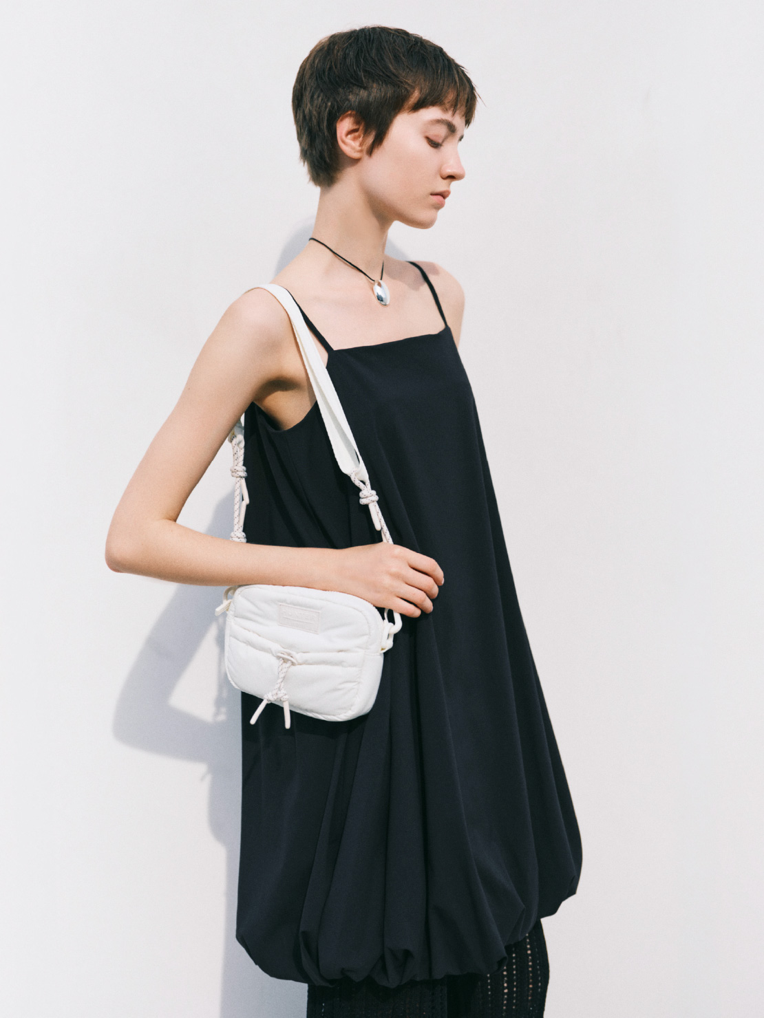 ブラック色のバルーンミニワンピースと白色の【emmi×HUNTER】クロスボディーを着用した女性のイメージ