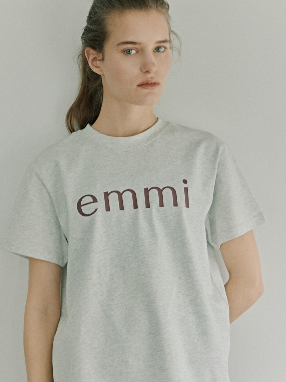 ライトグレー色のベーシックemmiロゴTシャツを着用したモデル画像