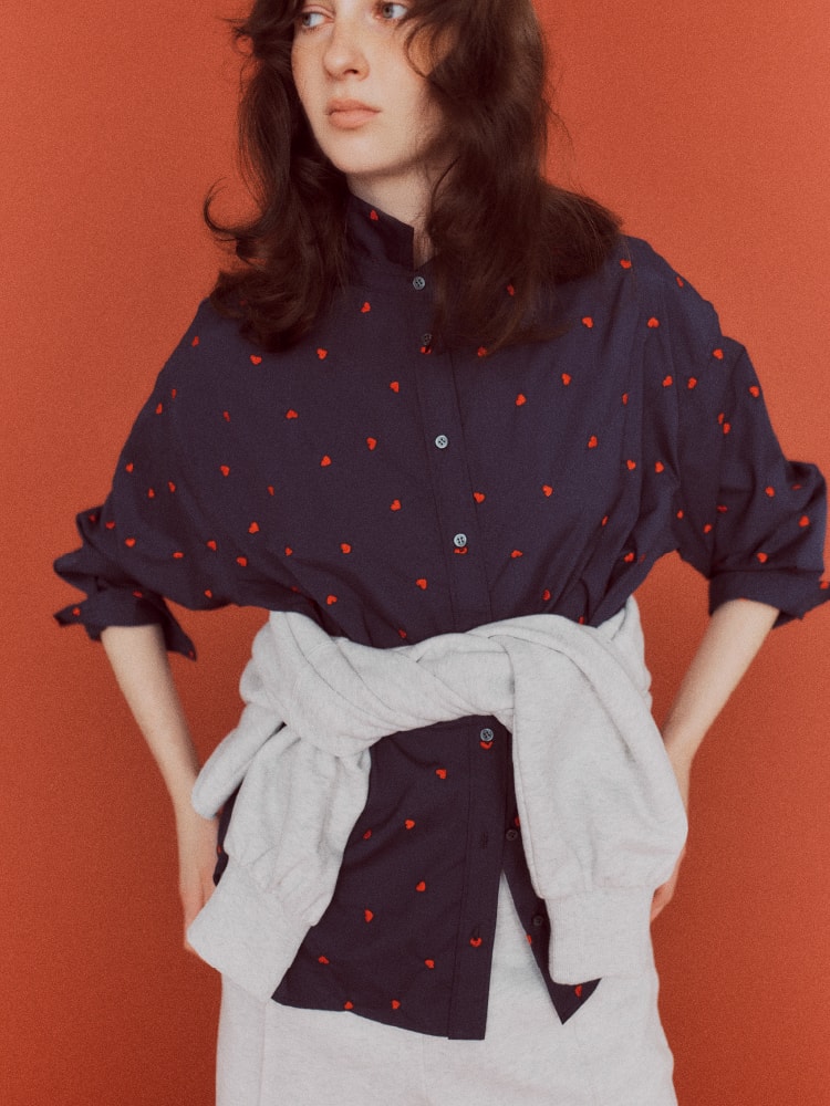 ハート柄のネイビーのトップスを着て腰に白いシャツを巻いた女性の画像