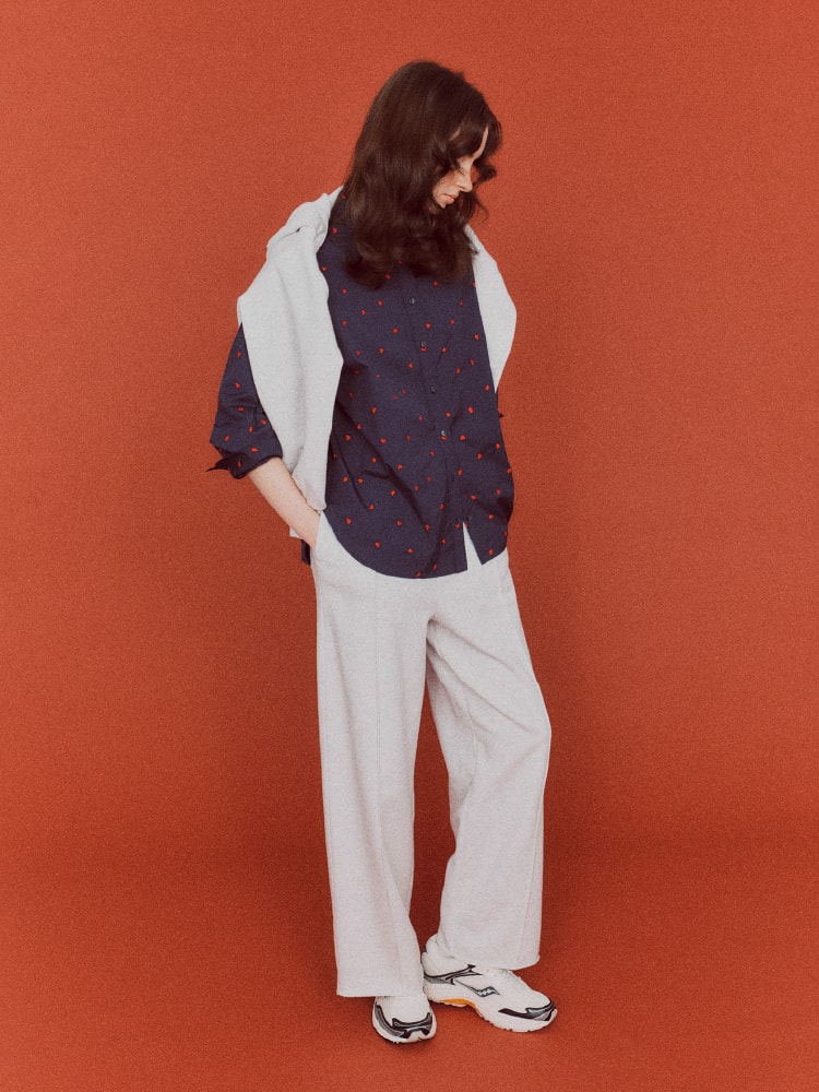 ハート柄のネイビーのトップスを着て白いシャツを首にかけた女性の画像