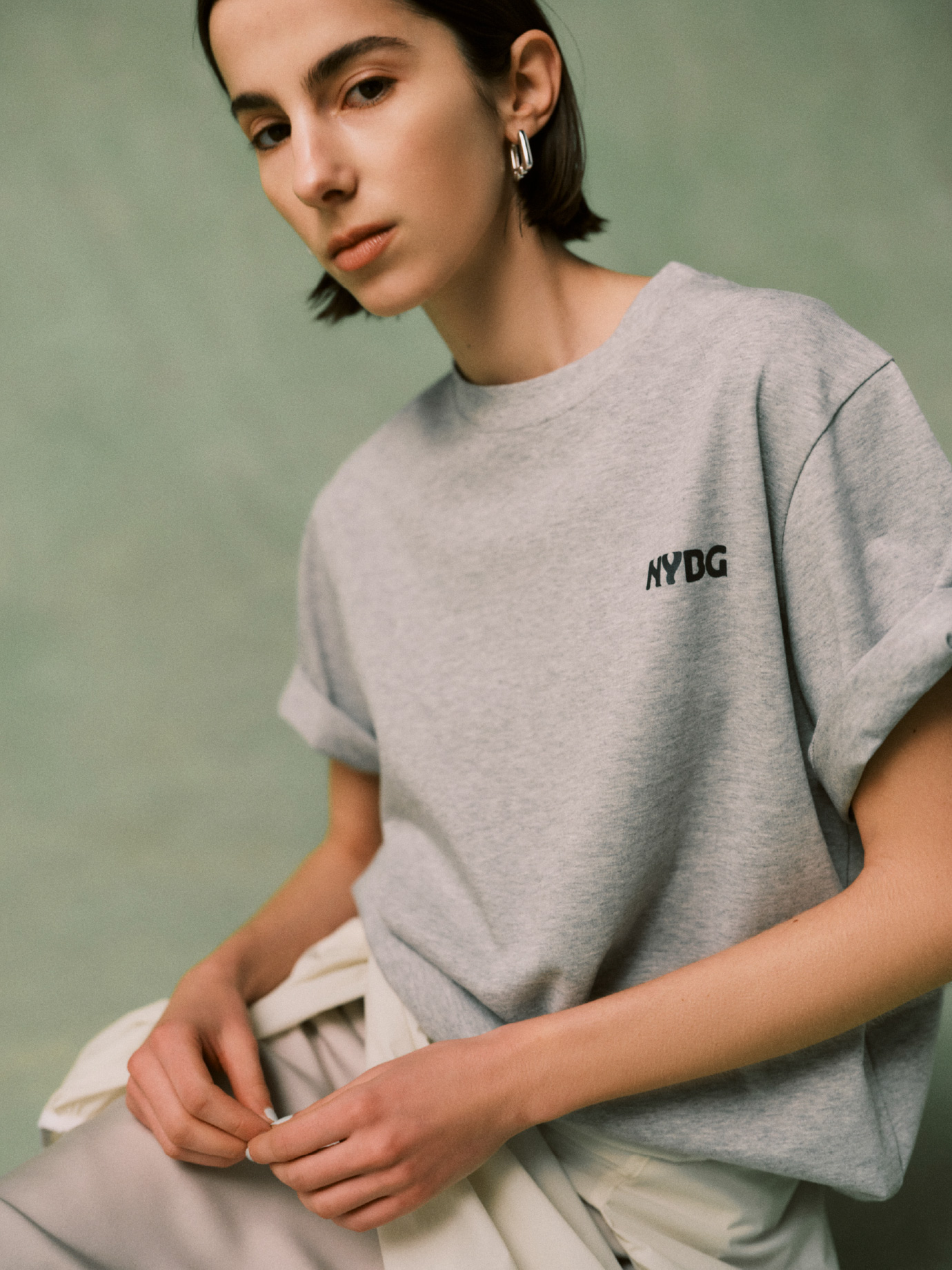 グレー色の【emmi×NYBG】グラフィックT、ロングワンタッチピアスを合わせたコーディネート