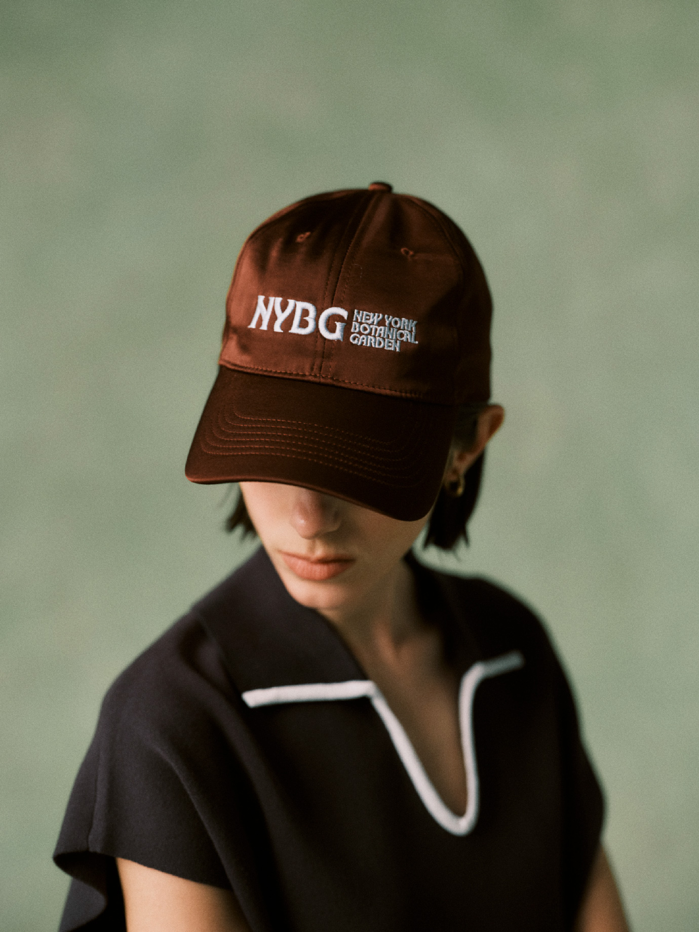 ブラウン色の【UV＋Cool】ポロニット、【emmi×NYBG】サテンロゴキャップを合わせたコーディネート